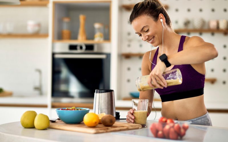 joven-atletica-feliz-desayunando-batido-frutas-cocina